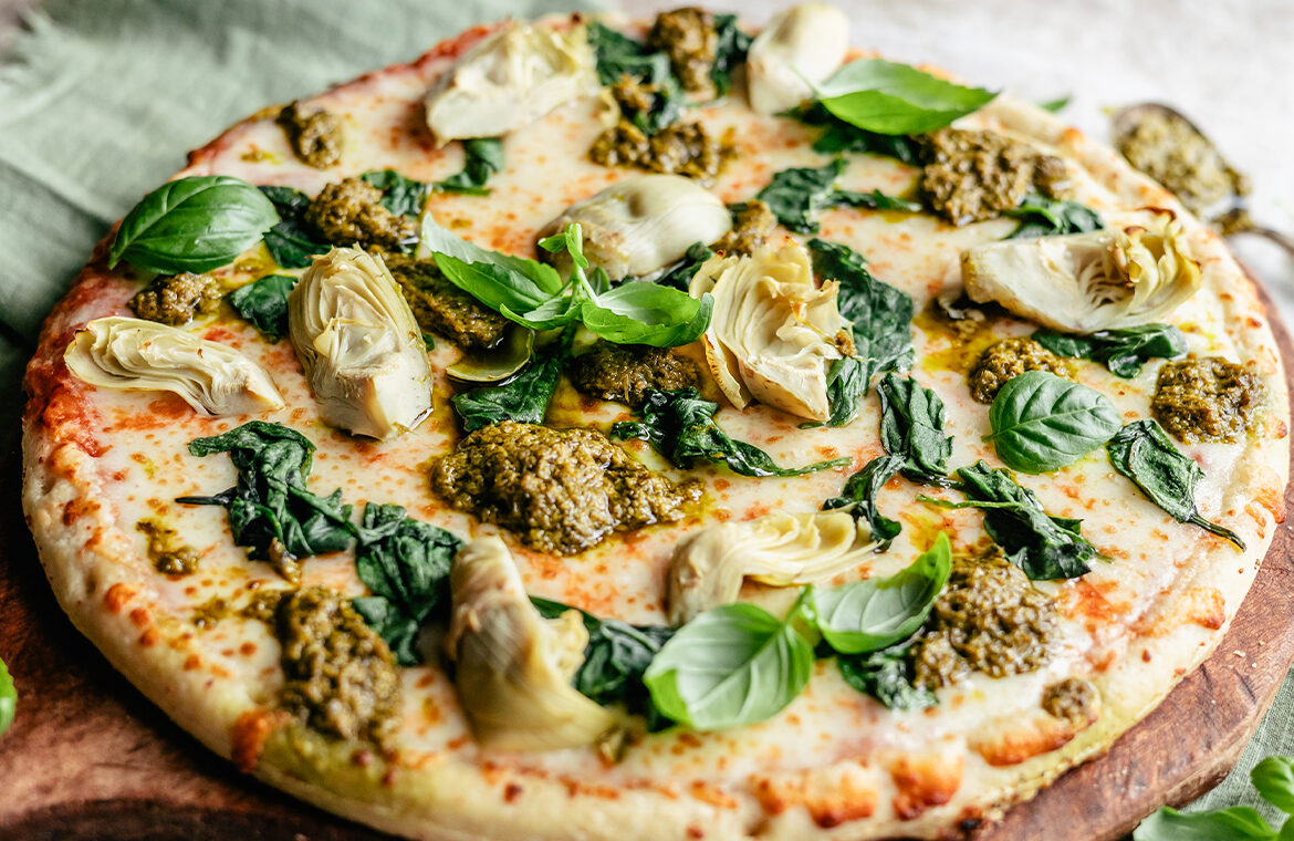 Pizza topped with spinach, artichoke, and pesto