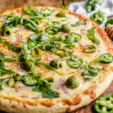 Baked pizza topped with jalapeno, arugula, olives, red onion