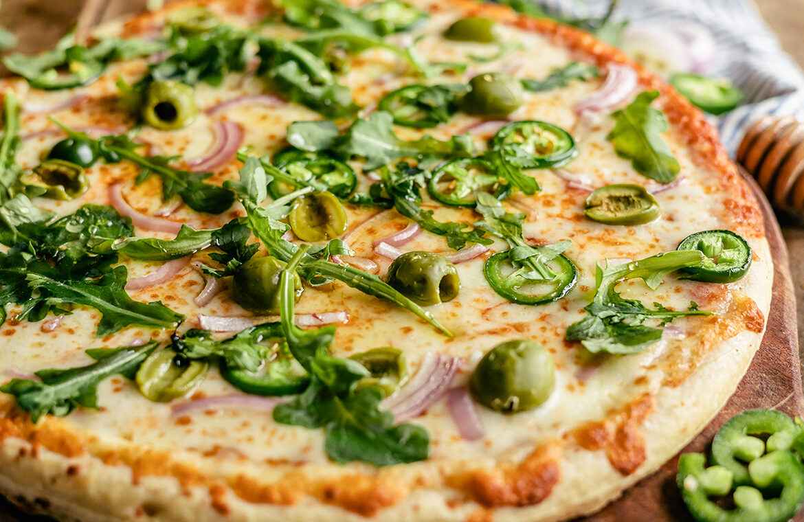 Baked pizza topped with jalapeno, arugula, olives, red onion