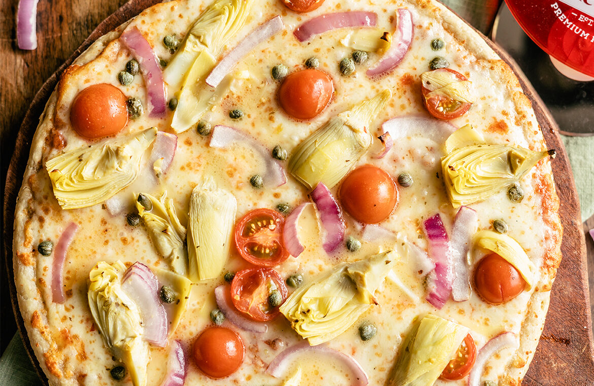 Pizza topped with artichoke, halved cherry tomatoes, and red onion