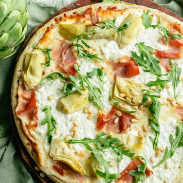pizza topped with arugula, artichoke, ricotta, prosciutto