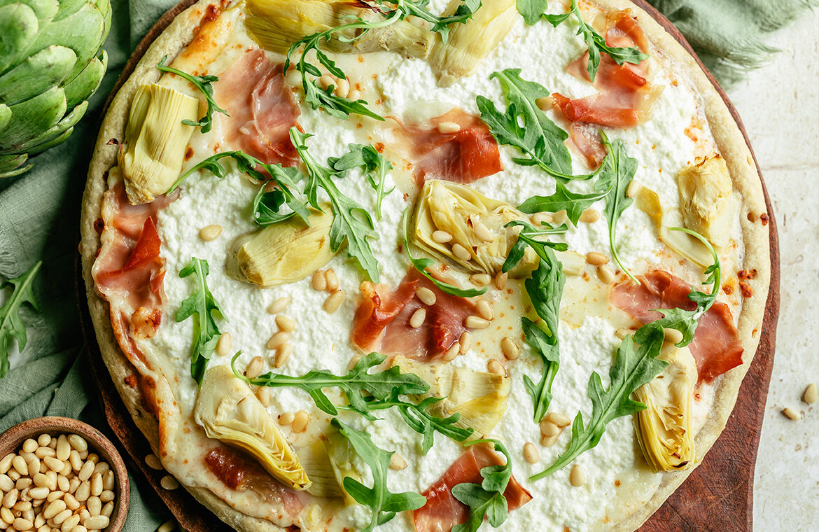 pizza topped with arugula, artichoke, ricotta, prosciutto