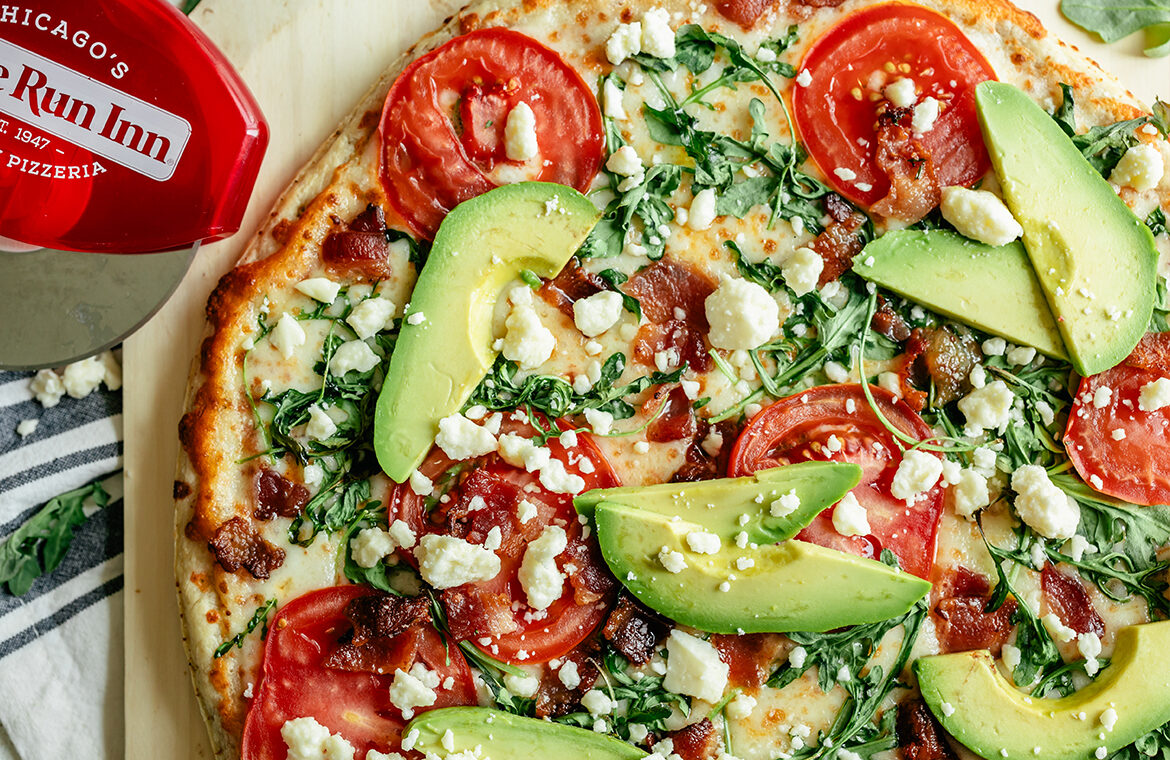 Cooked pizza topped with tomato, avocado, arugula, feta, and more