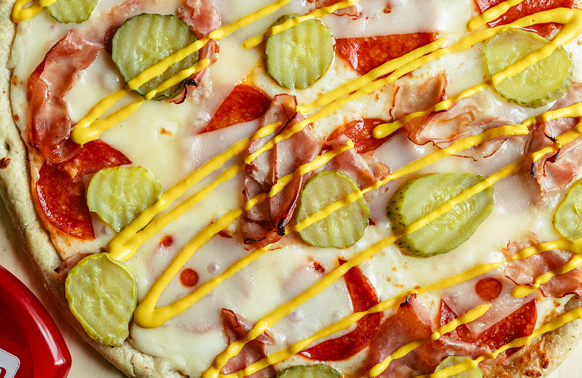 Pizza topped with ham, swiss, pickles, and mustard drizzle