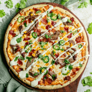 Pizza topped with Jalapenos, bacon, shaved steak, corn, and ranch drizzle