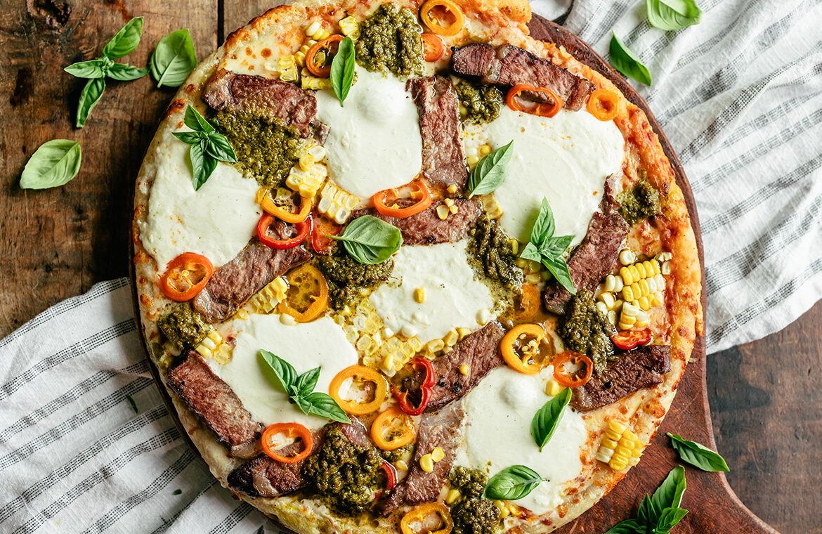 Grilled pizza topped with steak strips, burrata, corn, and more