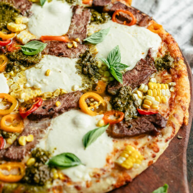 Grilled pizza topped with steak strips, burrata, corn, and more
