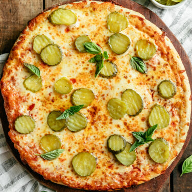 Baked cheese pizza topped with pickles, chili infused oil, and fresh basil