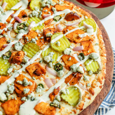 Baked pizza topped with buffalo chicken, pickles, blue cheese crumble, and ranch drizzle
