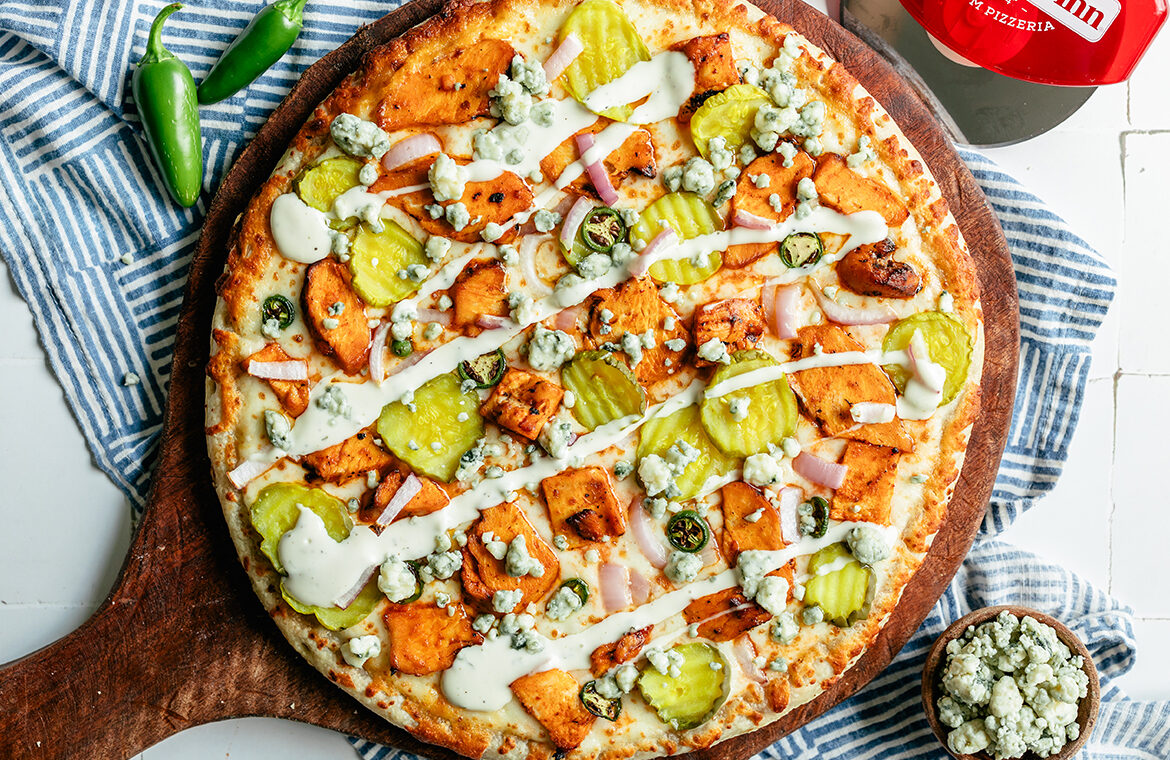 Baked pizza topped with buffalo chicken, pickles, blue cheese crumble, and ranch drizzle