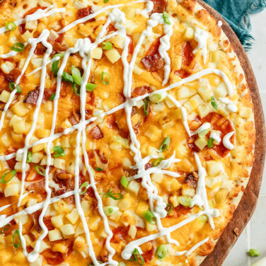 Baked pizza topped with potatoes and loaded with sour cream, green onions, and more