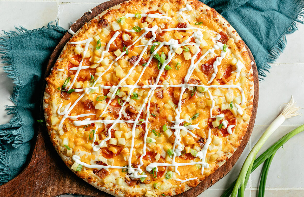 Baked pizza topped with potatoes and loaded with sour cream, green onions, and more