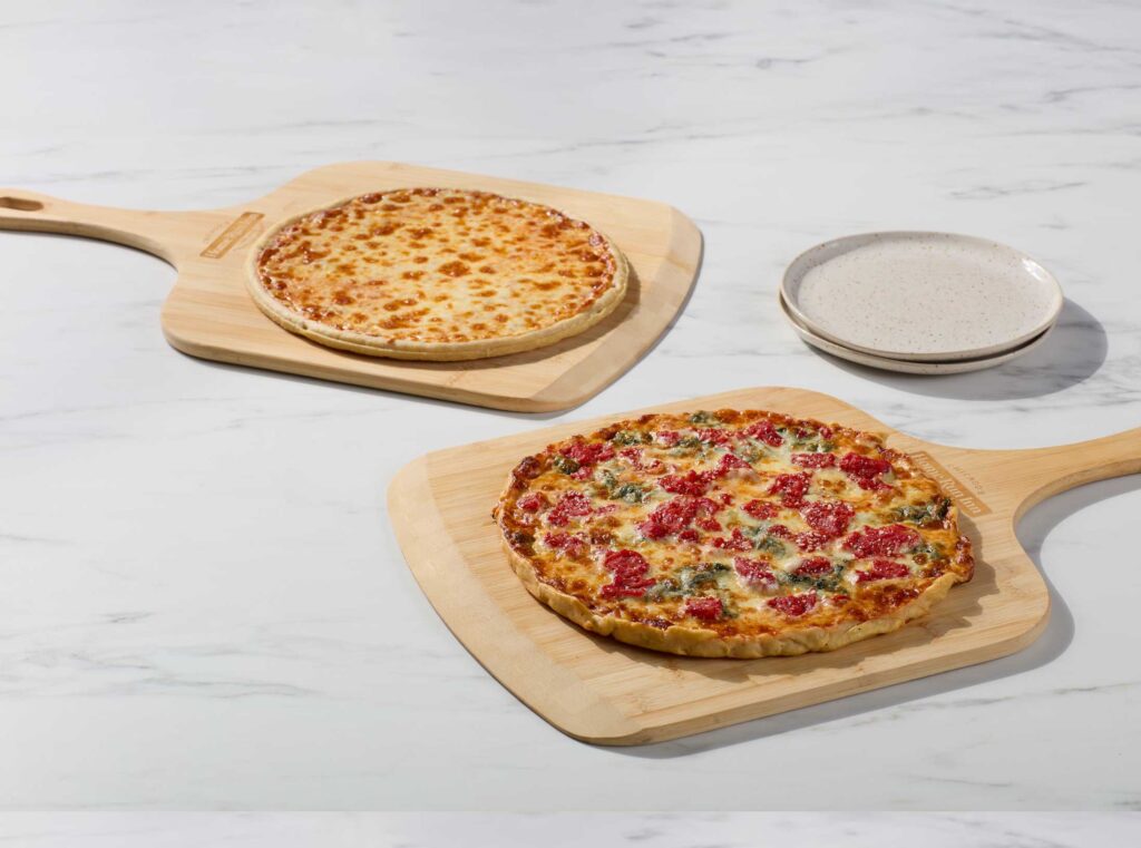two pizzas on paddles one lauras favorite with plum tomato and spinach the other cheese