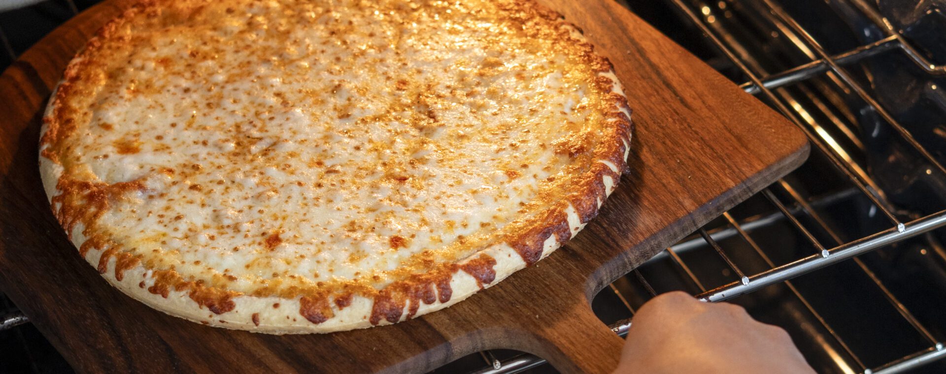 Freshly baked, golden-brown Home Run Inn thin-crust cheese pizza being pulled out of an oven on a wooden pizza peel.