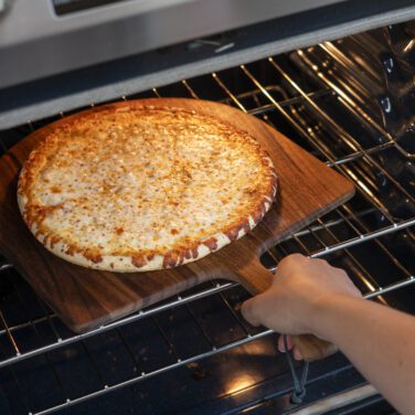 Freshly baked, golden-brown Home Run Inn thin-crust cheese pizza being pulled out of an oven on a wooden pizza peel.