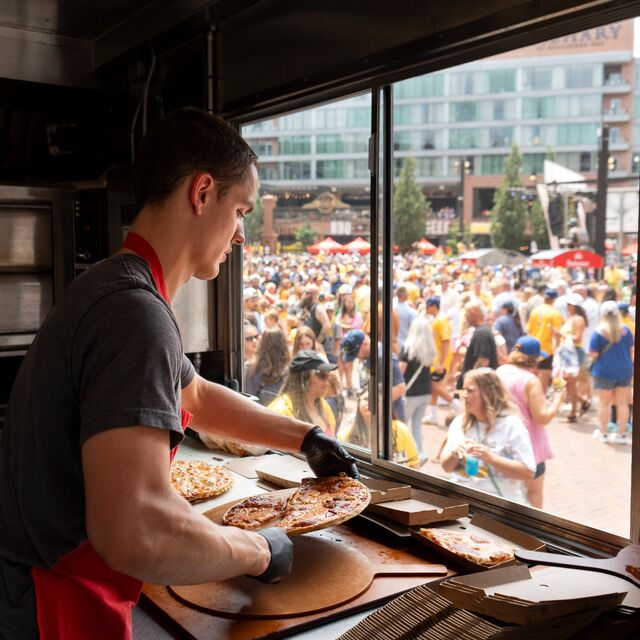 Home Run Inn employee packaging pizza in the food truck with a crowd forming outside of the window